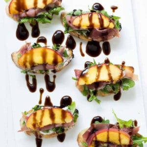 Platter of grilled peach crostini with goat cheese, arugula, prosciutto and balsamic drizzle.