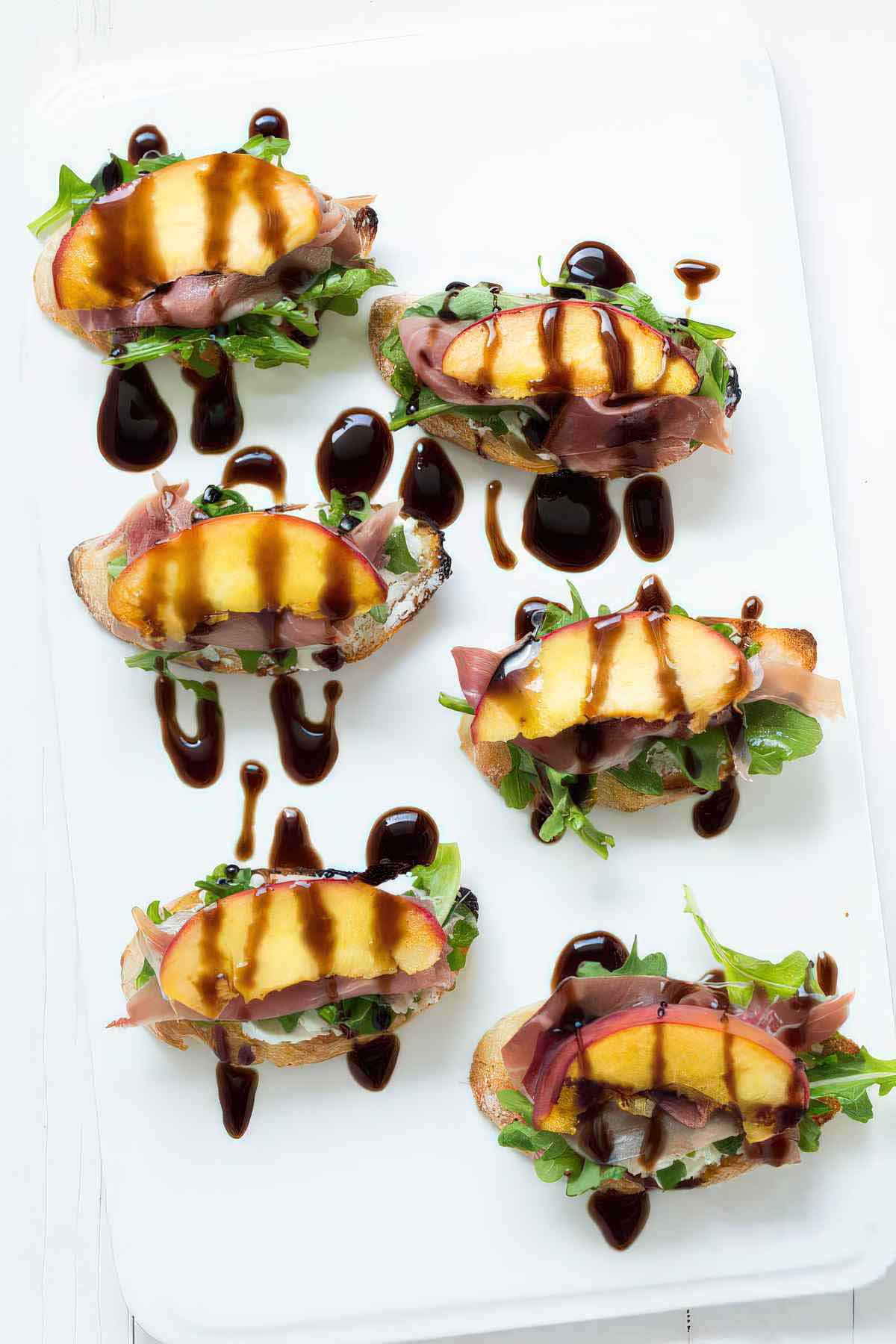 Platter of grilled peach crostini with goat cheese, arugula, prosciutto and balsamic drizzle.