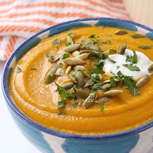 Creamy butternut squash and red lentil soup topped with Greek yogurt, pepitas and chopped parsley in a blue patterned bowl.