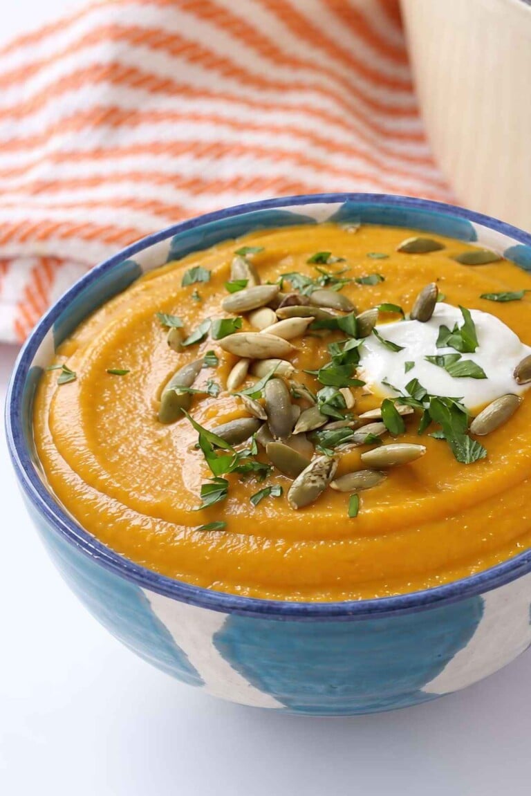 Creamy butternut squash and red lentil soup topped with Greek yogurt, pepitas and chopped parsley in a blue patterned bowl.