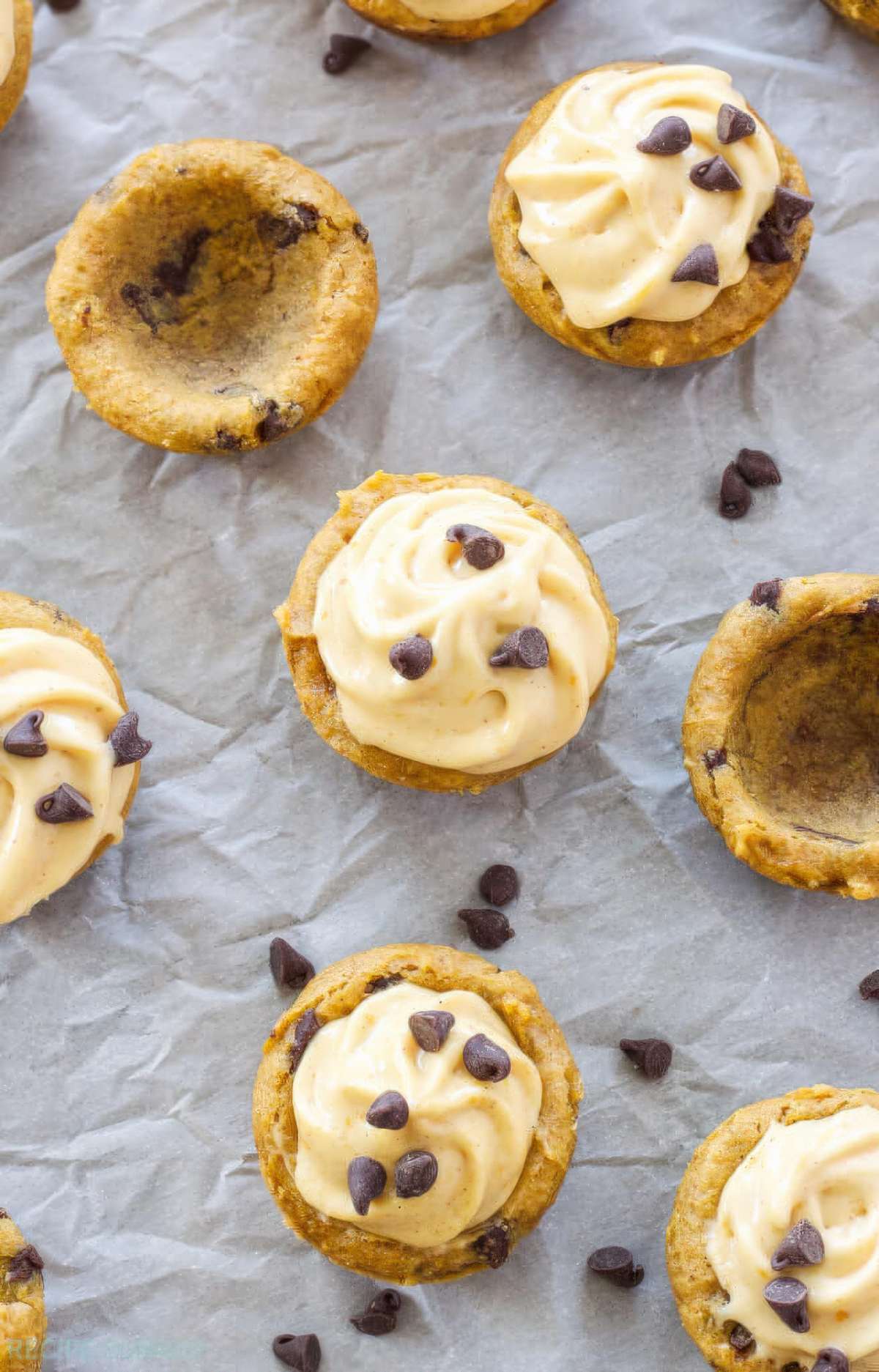 Overhead view of filled and unfilled pumpkin chocolate chip cookie cups, showing the wells that hold the pumpkin cream cheese frosting.