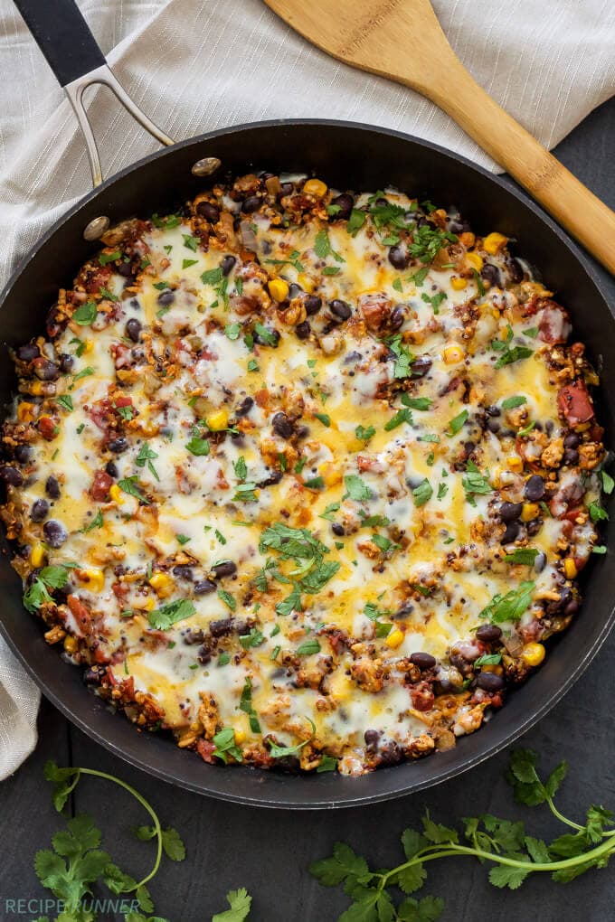 mexican quinoa with melted cheese and chopped cilantro in a dark skillet