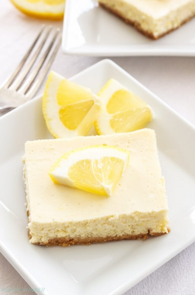 A slice of lemon cheesecake on a white plate with a lemon slice on the side