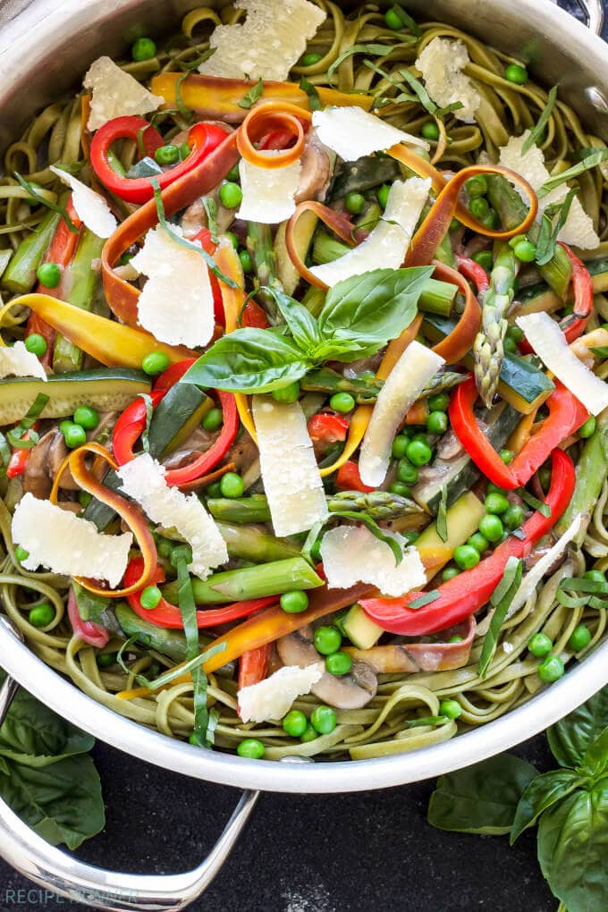 A close up of pasta primavera loaded with spring vegetables, topped with parmesan and basil. 