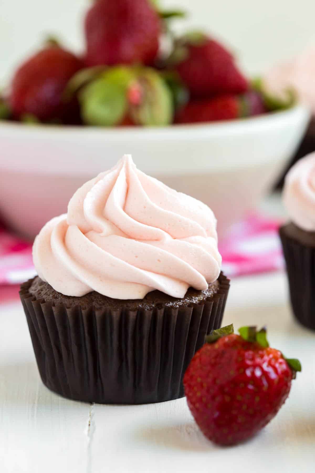 one chocolate strawberry cupcake sitting in front of a bowl of strawberries
