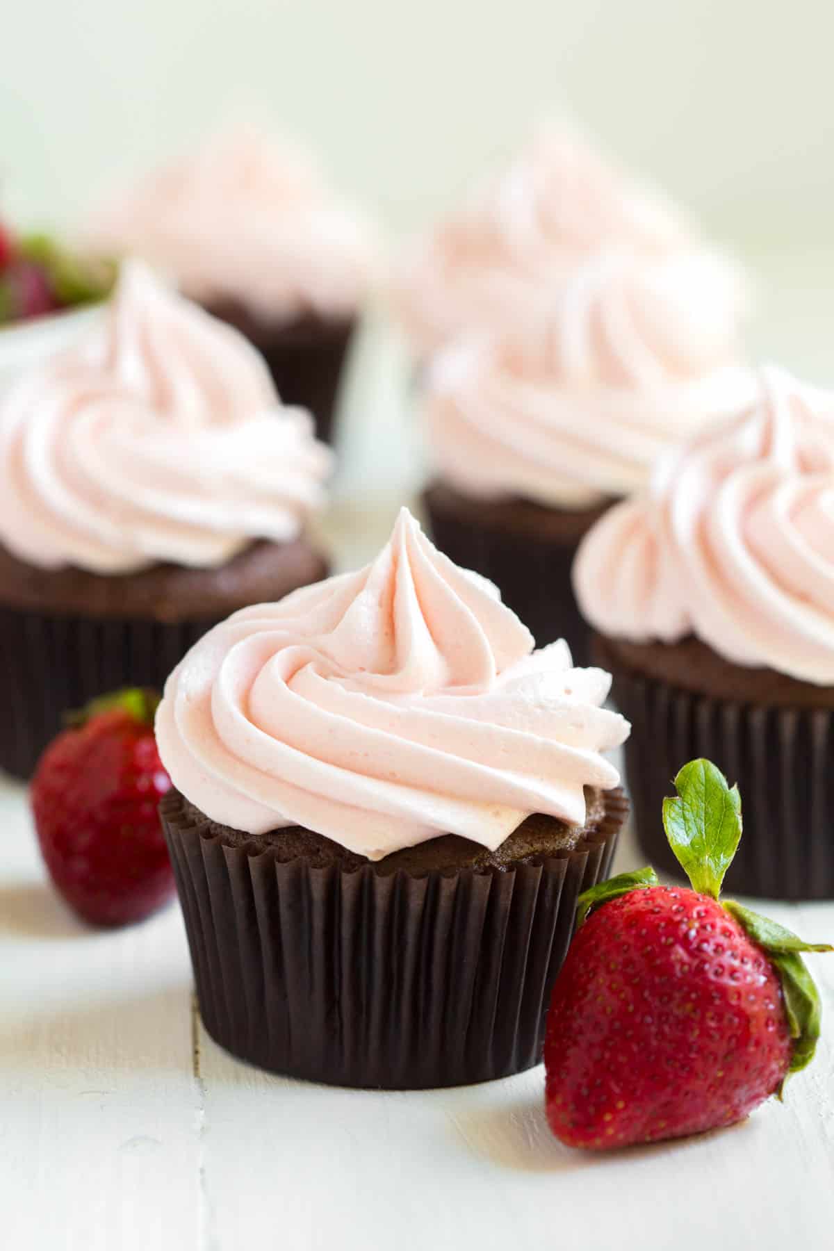 chocolate cupcakes with strawberry frosting sitting on a white countertop