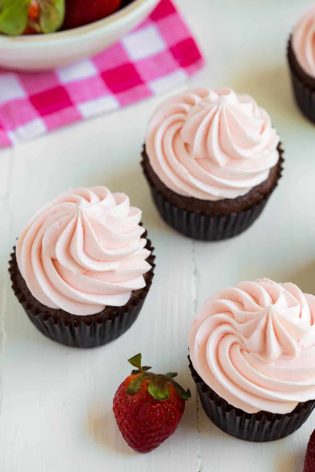 three chocolate cupcakes with strawberry frosting sitting on a white table