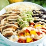 Chicken taco bowl with chipotle lime chicken, rice, black beans, mango salsa, guacamole, and creamy mango chipotle sauce