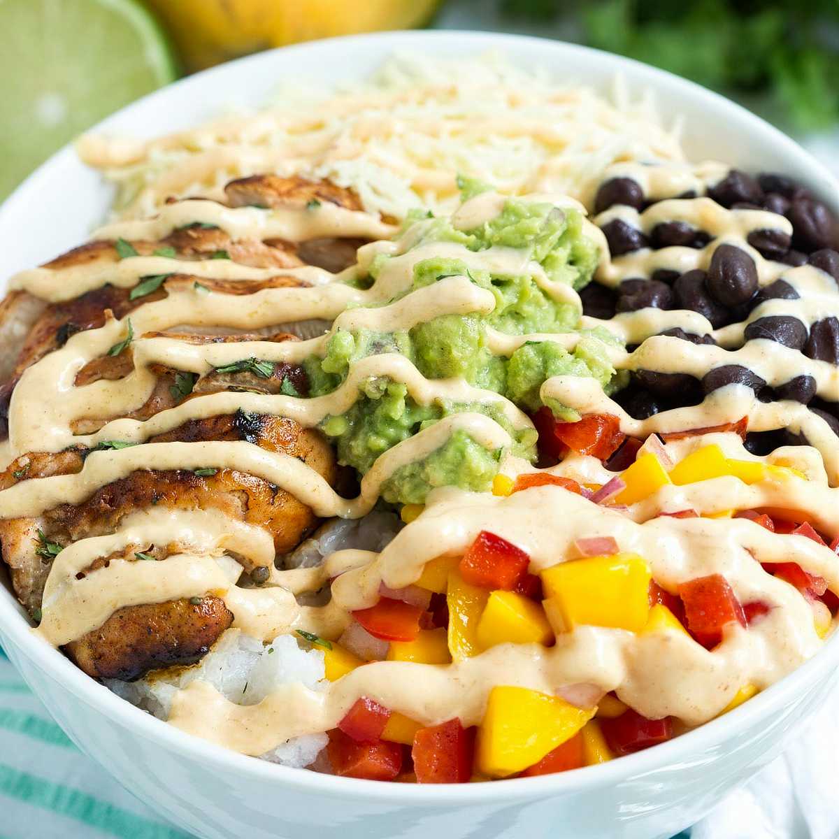 Chicken taco bowl with chipotle lime chicken, rice, black beans, mango salsa, guacamole, and creamy mango chipotle sauce