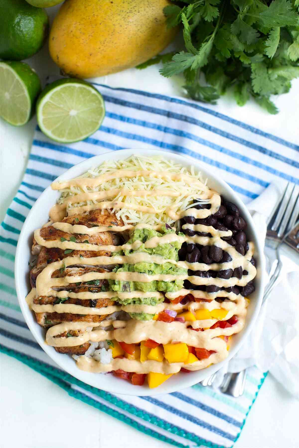 Overhead view of chicken taco bowl with mango salsa, black beans, guacamole, rice, and creamy chipotle mango sauce