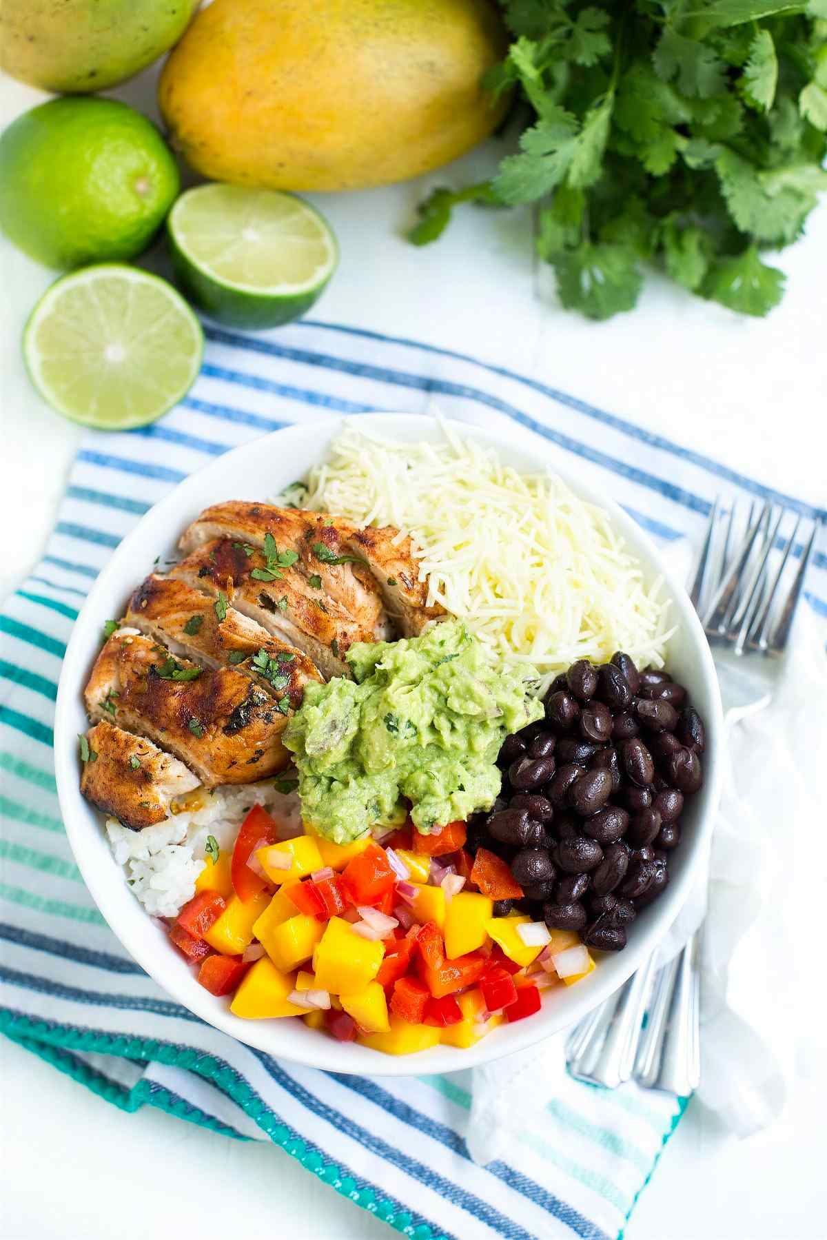 Chipotle lime chicken taco bowl with rice, black beans, shredded cheese, guacamole, and fresh mango salsa