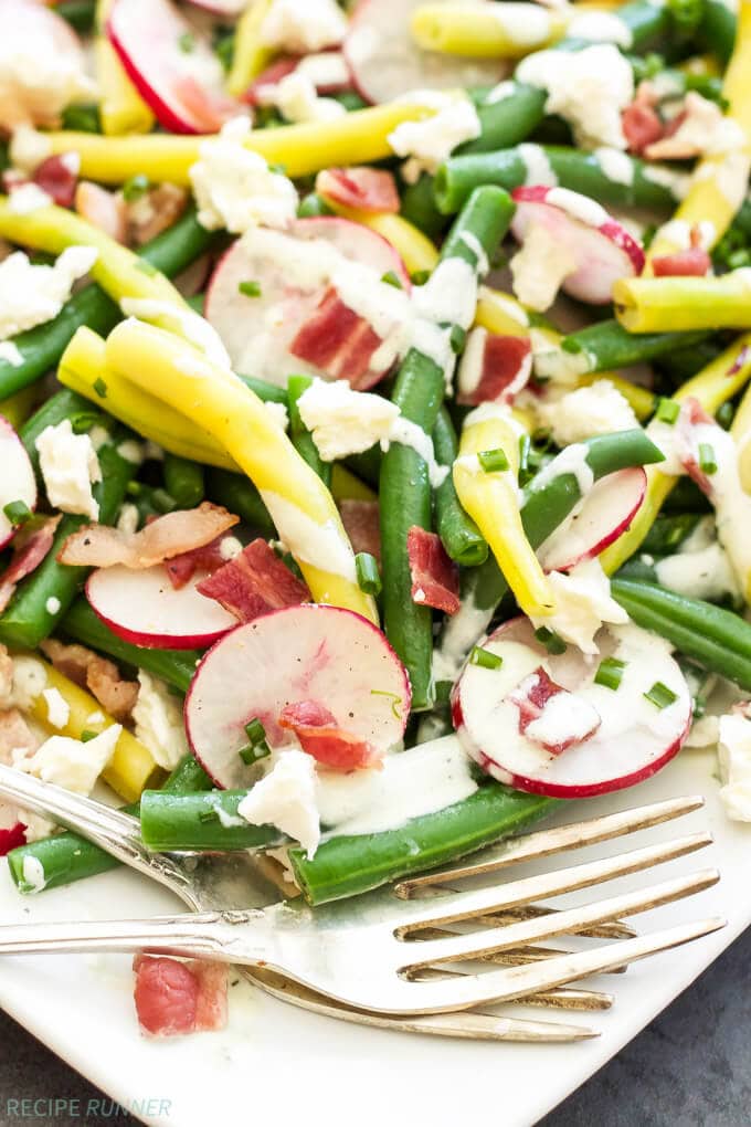 green bean and feta salad with bacon and radishes on a white plate with a fork