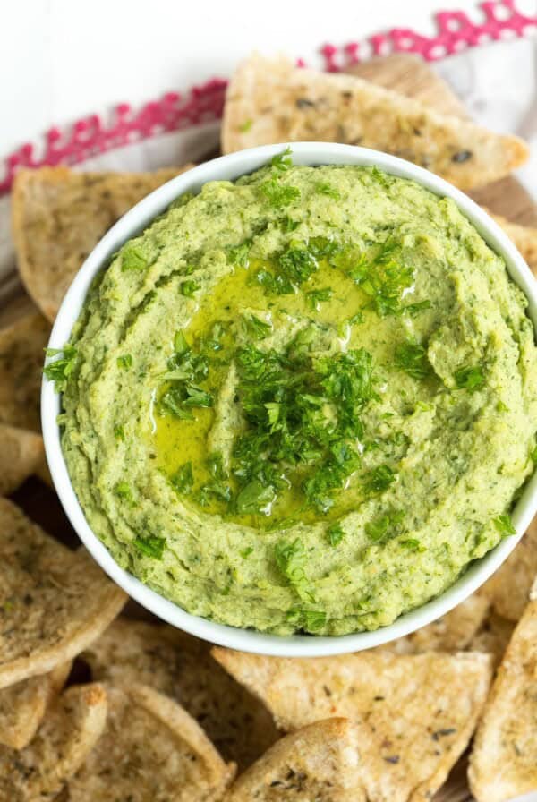up close picture of lemon hummus on a table with seasoned pita chips and lemon slices.