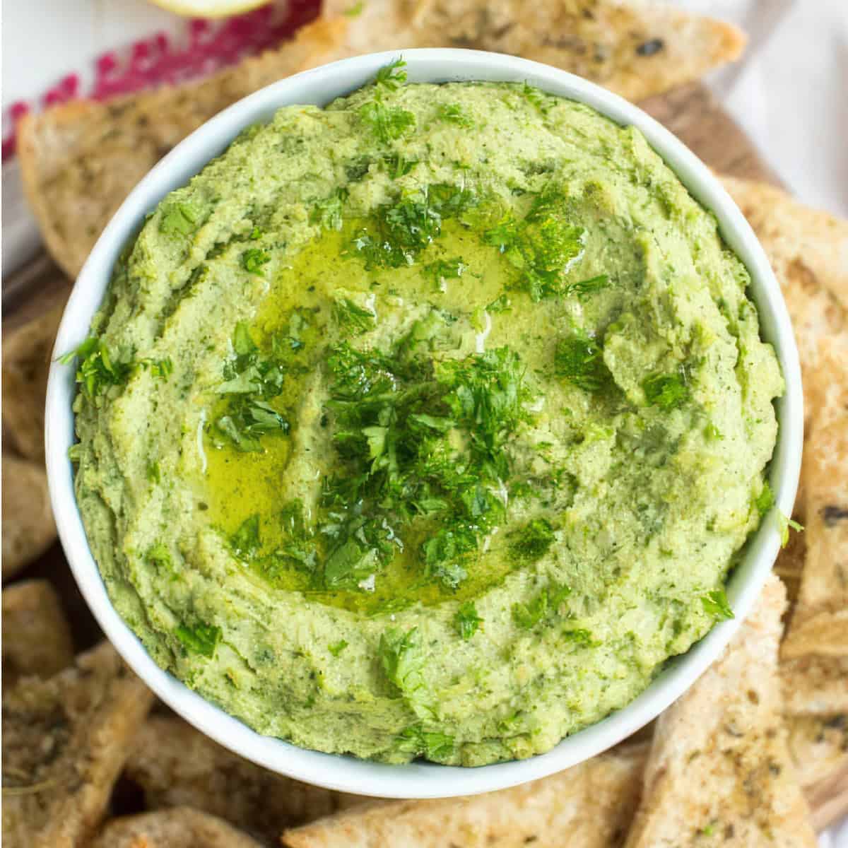 up close picture of lemon hummus on a table with seasoned pita chips and lemon slices.