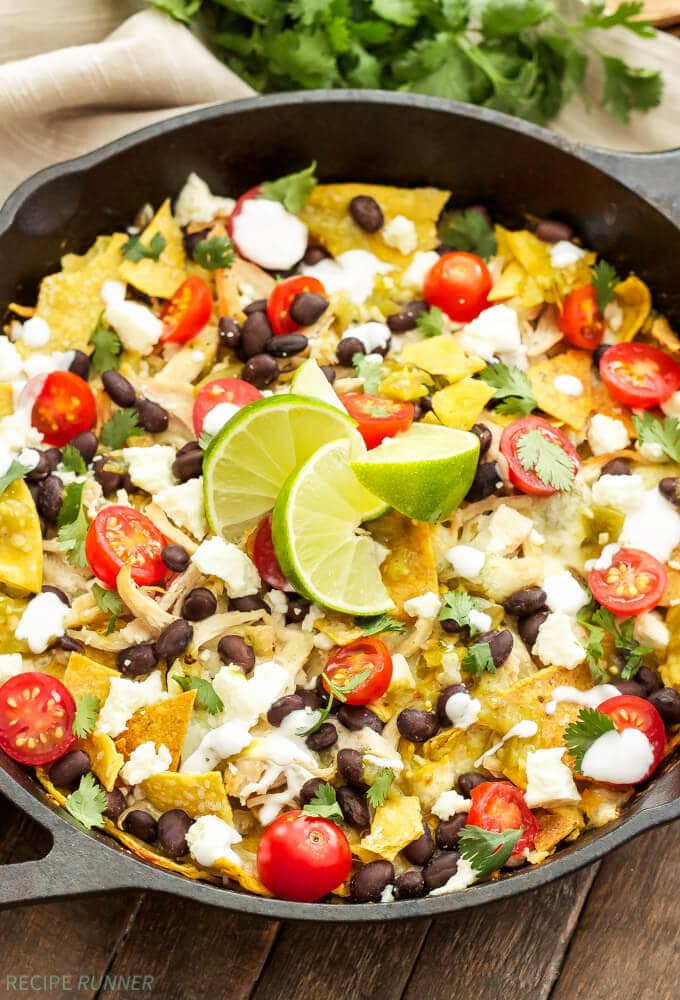 chicken chilaquiles with toppings and lime wedges in a cast iron skillet