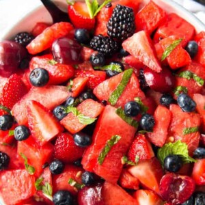 A large bowl of watermelon chunks, berries and cherries with mint.