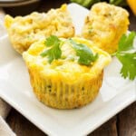 Cheesy zucchini quinoa egg muffins baked in a muffin tin with melted cheese on top served on a white plate