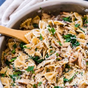 a wooden spoon scooping out spinach and mushroom pasta