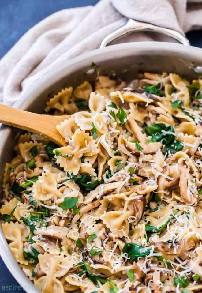 a wooden spoon scooping out spinach and mushroom pasta