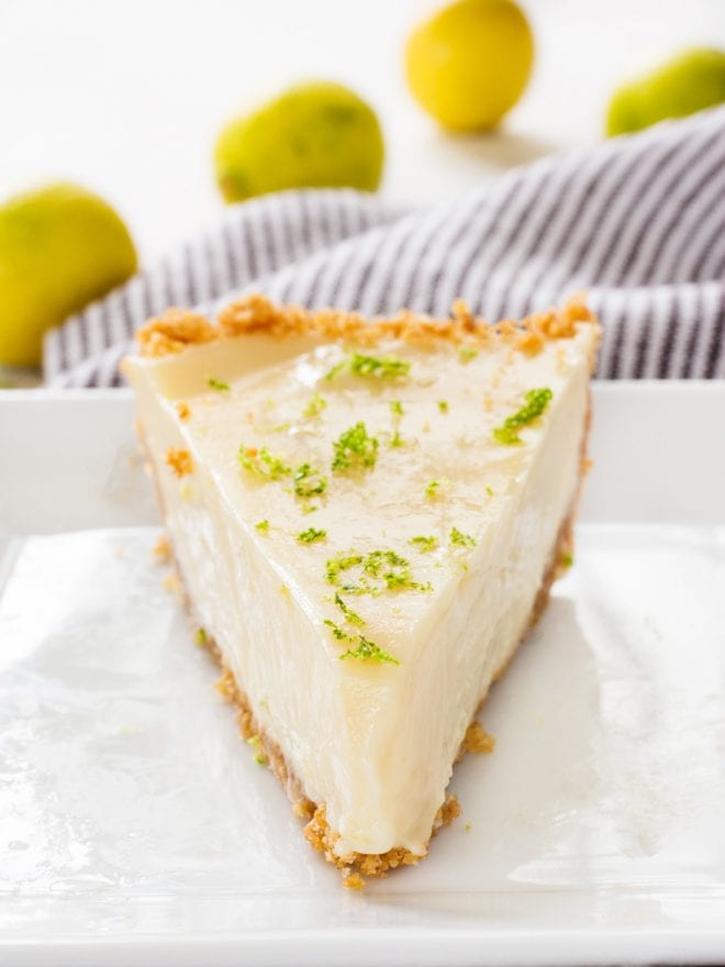 A large slice of key lime pie sitting on a white plate with lime zest on top.