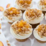 Peach pie cupcakes sit on top of a cupcake stand with slices of fresh peaches off to the side.