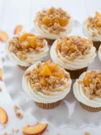 Peach pie cupcakes sit on top of a cupcake stand with slices of fresh peaches off to the side.