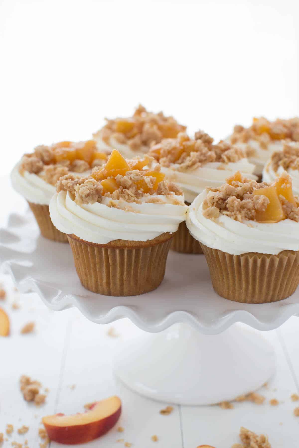 Peach pie cupcakes with vanilla bean frosting and peach filling on top of a white serving plate.