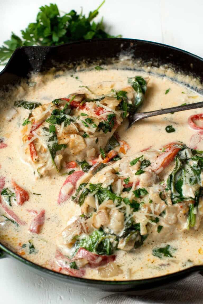 Close up of creamy chicken with bacon, spinach, roasted red peppers, and parmesan in a rich garlic sauce
