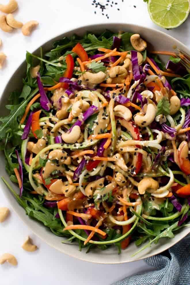 Zucchini Noodle Pad Thai Salad is made with the freshest, raw ingredients including carrots, zucchini, cabbage, arugula, red peppers and a creamy sesame-cashew dressing! #salad #healthy #recipe #raw #cashew #vegan #thai
