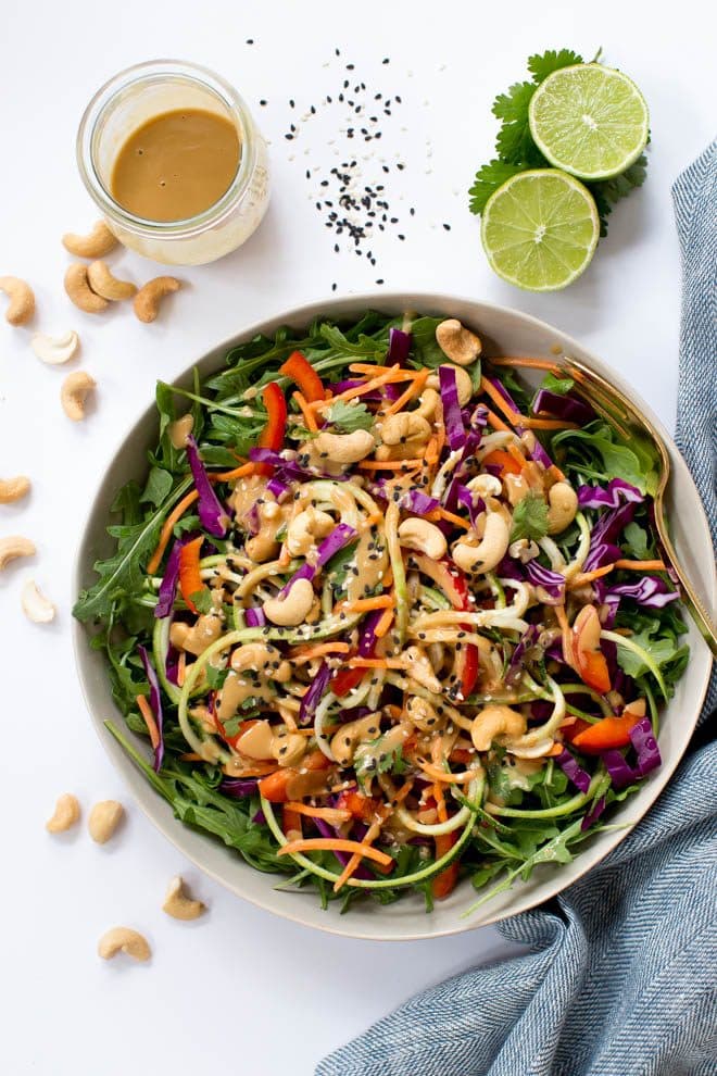 Zucchini Noodle Pad Thai Salad with Sesame-Cashew Dressing is made with the freshest, raw ingredients including carrots, zucchini, cabbage, arugula, red peppers and a creamy sesame-cashew dressing! #salad #healthy #recipe #raw #cashew #vegan #thai