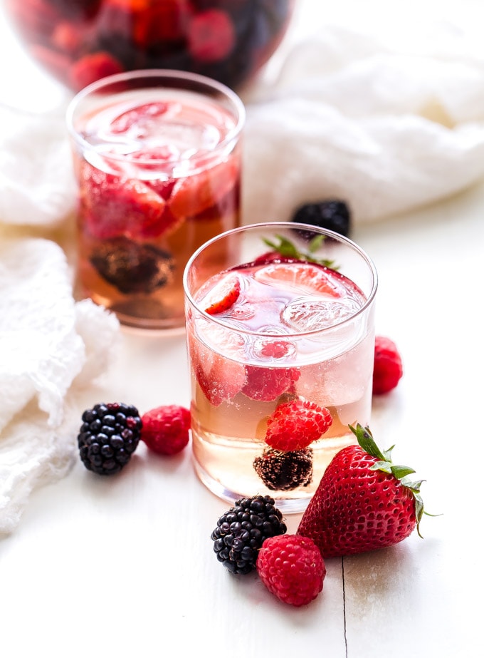 two clear glasses filled with rosé sangria and a few fresh berries sitting on a white table