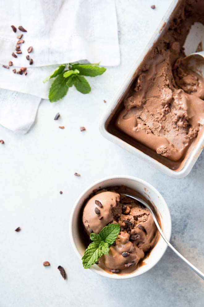 three scoops of chocolate coconut milk ice cream in a bowl with the container of ice cream on the side