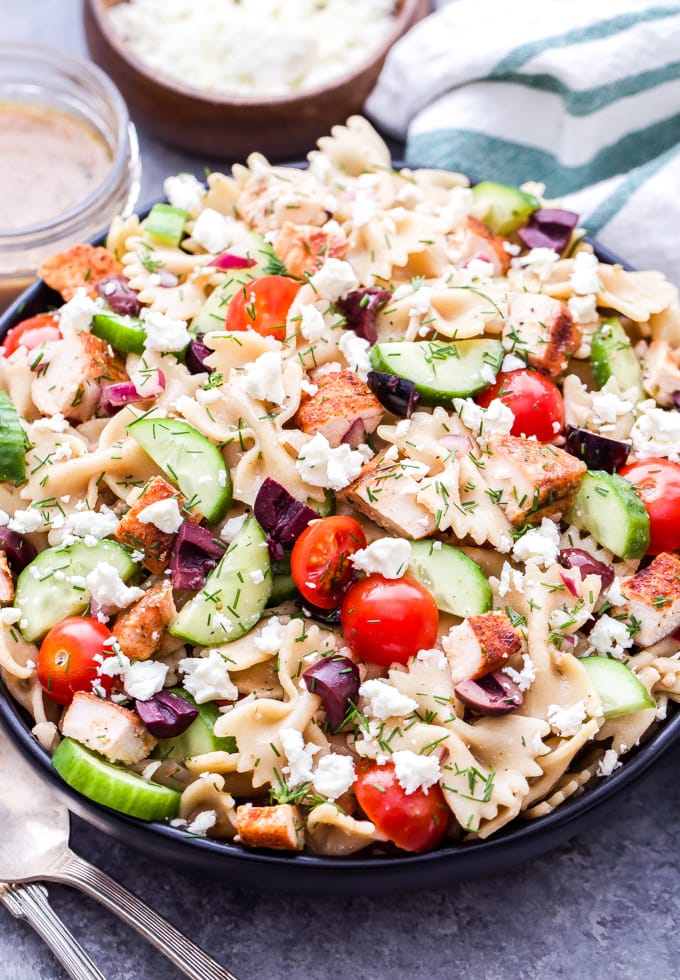 a bowl filled with pasta, chicken, cucumbers, tomatoes, olives and other ingredients to make greek chicken pasta salad