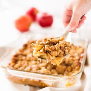 Scoop of apple crisp with a large baking dish of the apple crisp.