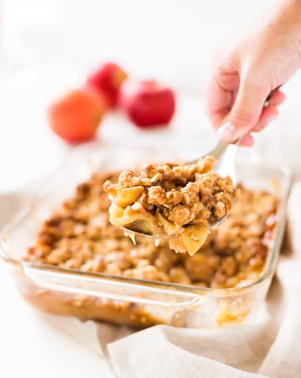Scoop of apple crisp with a large baking dish of the apple crisp.