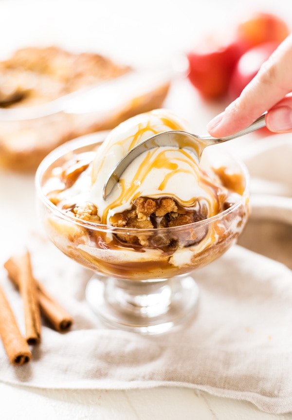 Bowl of apple crisp with ice cream and caramel sauce.