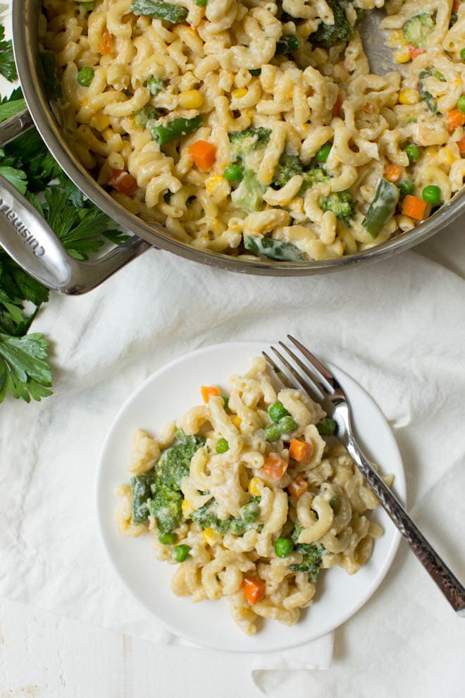 A pan of veggie mac and cheese sits to the side of a plate filled with mac and cheese.