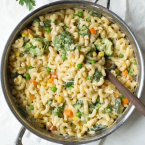 Overhead view of a skillet filled with cheesy macaroni and mixed vegetables like broccoli, peas, and carrots.