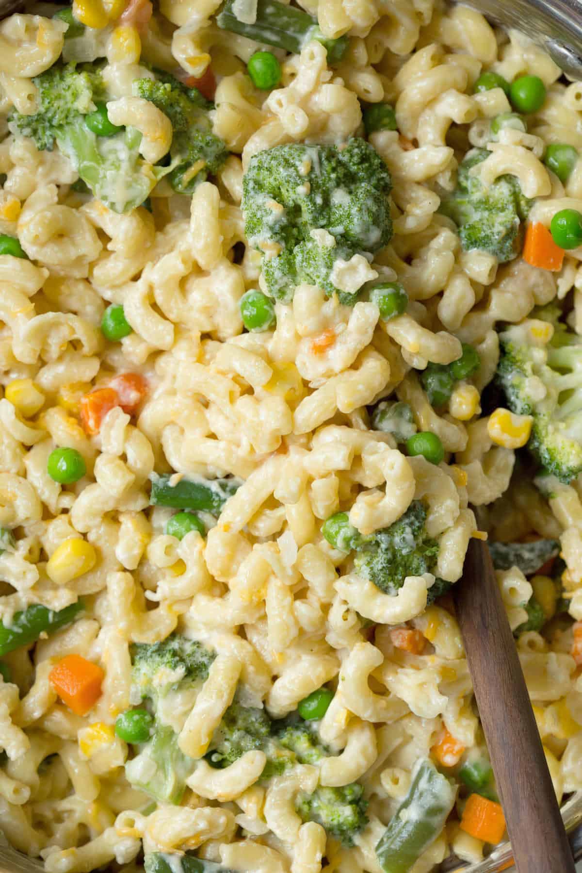 A close-up view of cheesy elbow macaroni mixed with broccoli, peas, carrots, and corn in a creamy sauce.