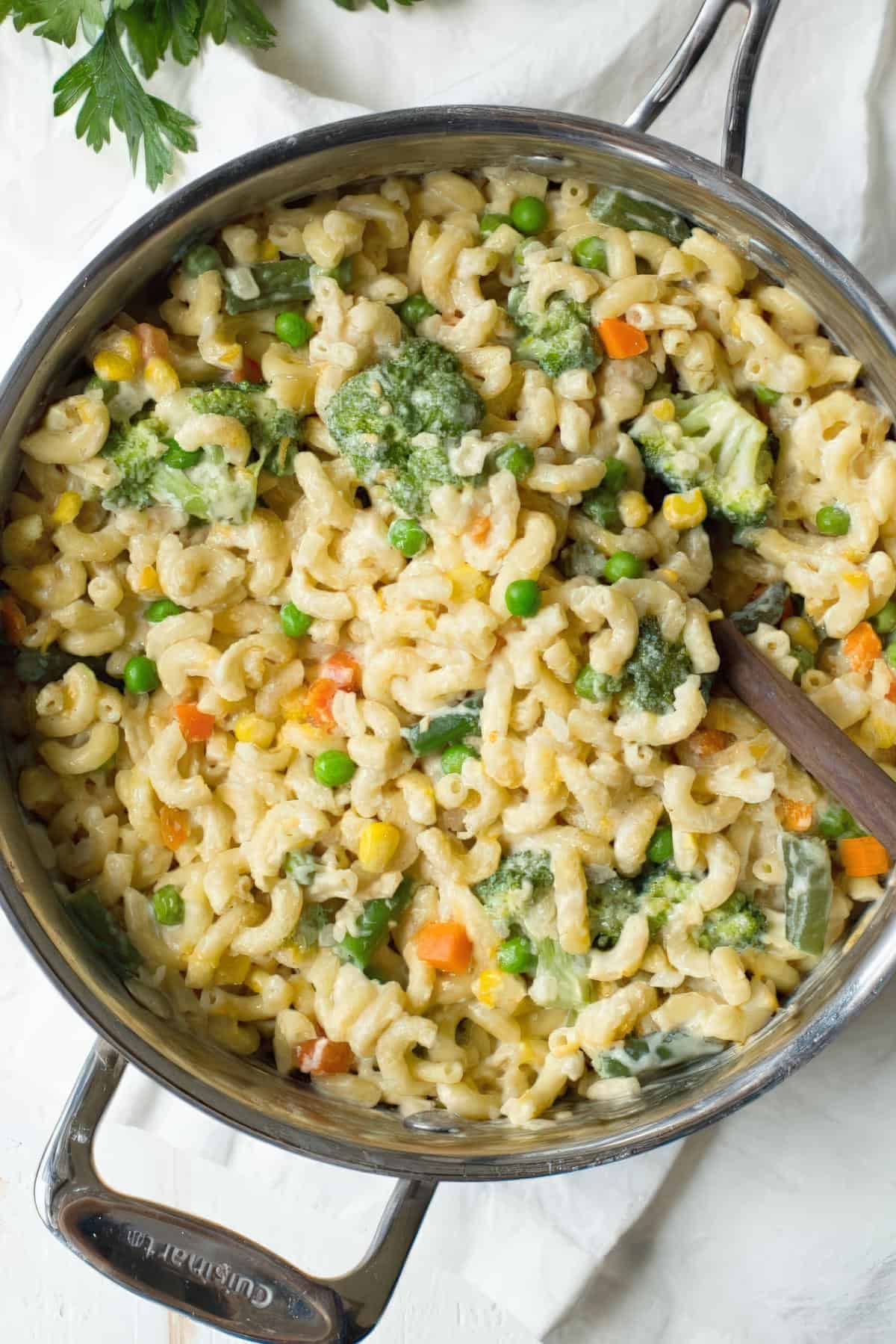 Overhead view of a skillet filled with cheesy macaroni and mixed vegetables like broccoli, peas, and carrots.