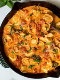 Creamy tomato basil tortellini pasta is served in a skillet and garnished with basil and grated parmesan.