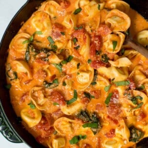 Creamy tomato basil tortellini pasta is served in a skillet and garnished with basil and grated parmesan.