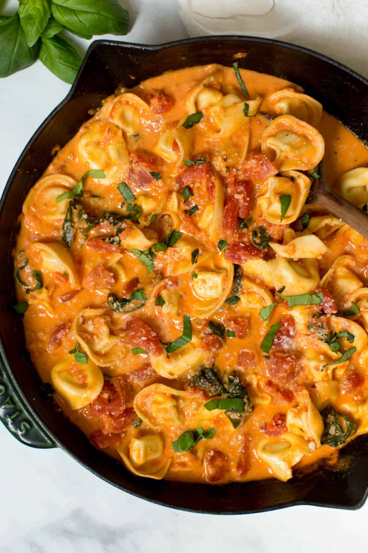 Creamy tomato basil tortellini pasta is served in a skillet and garnished with basil and grated parmesan. 