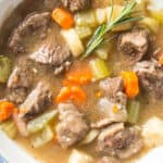 A large white bowl filled with Instant Pot Beef Stew and a sprig of rosemary sits on top for the garnish.