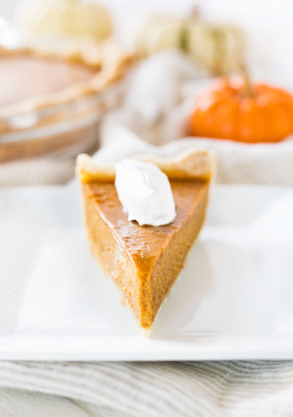 a slice of pumpkin pie on a white plate with a dollop of whipped cream
