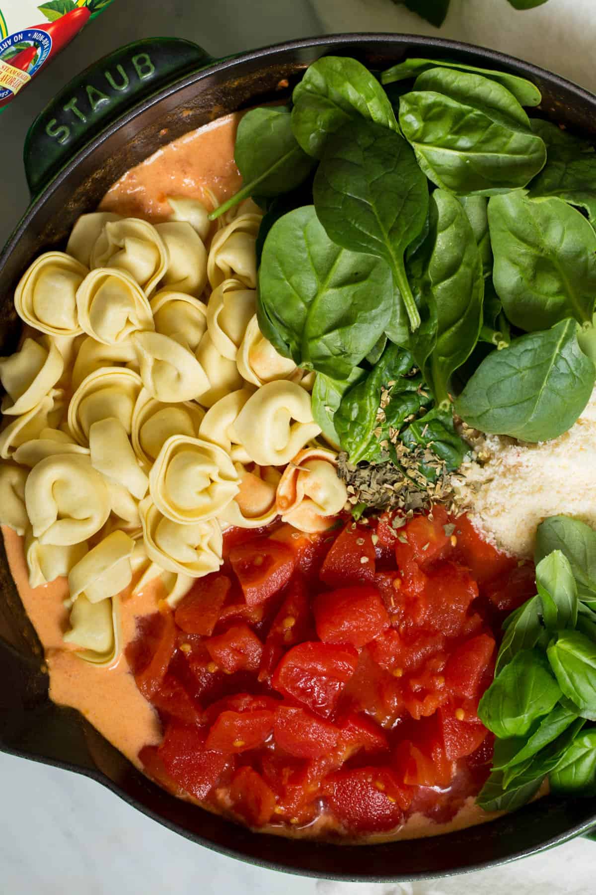 The fresh tortellini, spinach, diced tomatoes, basil and parmesan cheese sit in a skillet before stirring everything together and cooking.