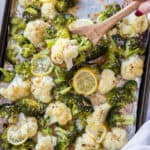 A spoon scooping roasted broccoli and cauliflower off the pan.