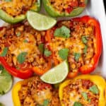 Six stuffed bell peppers sit in a white baking dish for serving.