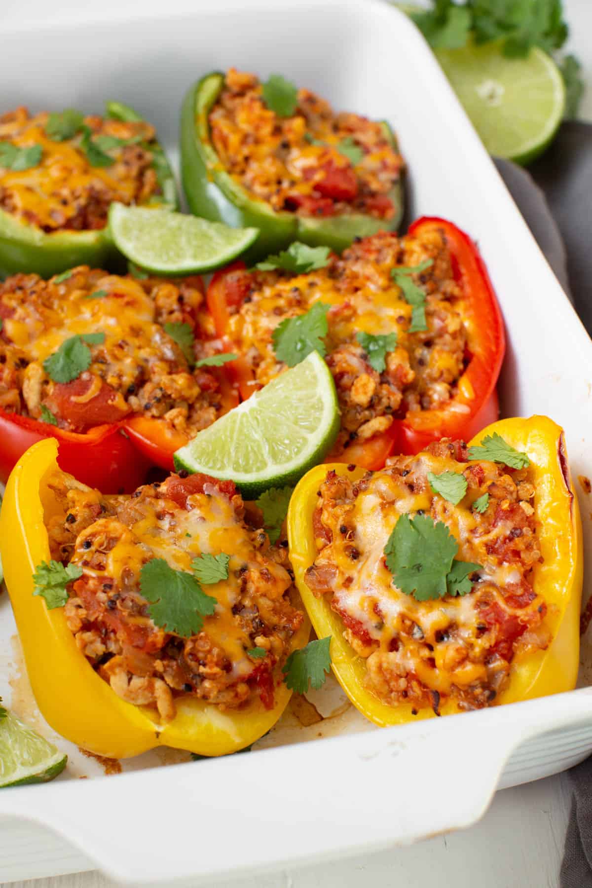 Cooked stuffed ground turkey bell peppers in a white baking dish garnished with cilantro and slices of lime.