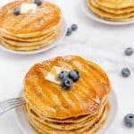 three stacks of blueberry buttermilk pancakes sitting on white plates on a counter